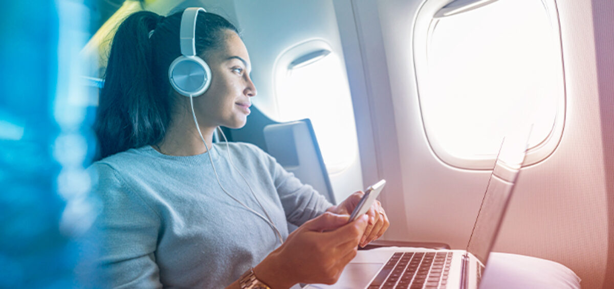 Woman on plane with laptop, cellphone, earphones